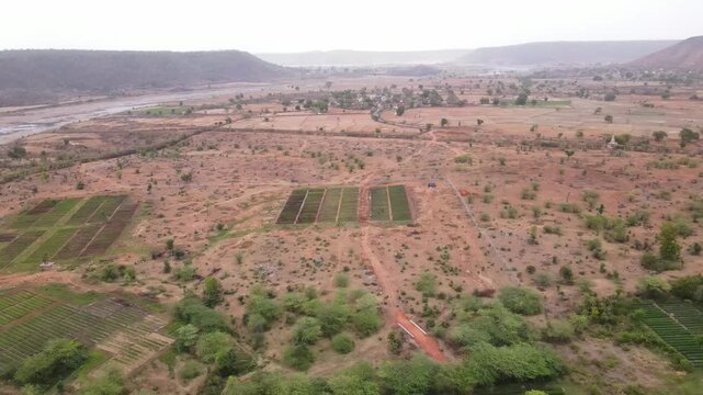 Cinematic drone pullback revealing agricultural nursery plots, dry countryside, rural settlement, valley, and distant hills in central India, highlighting sustainable farming landscapes.