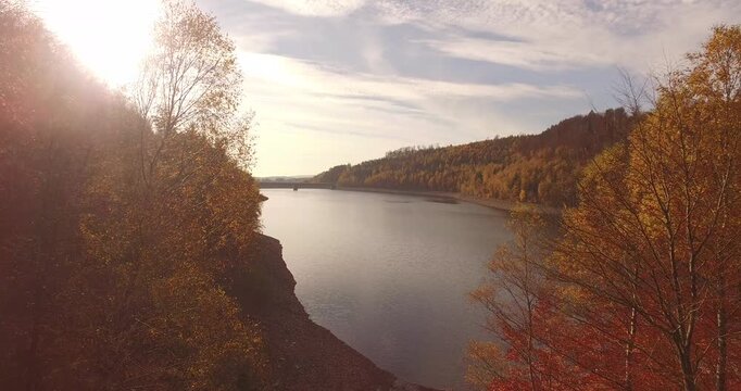 Drone shot flying along a winding river valley with dense green and yellow autumn trees on slopes