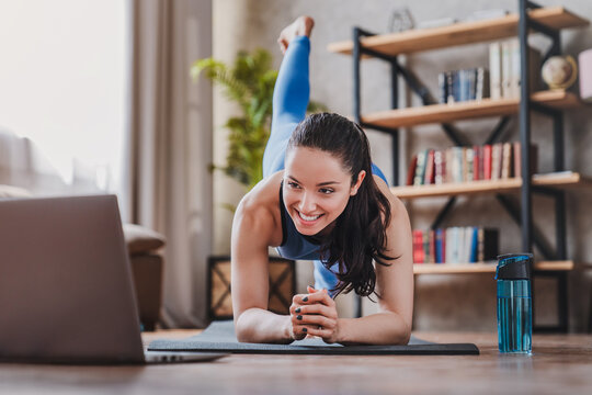 Fit woman doing yoga plank and watching online tutorials on laptop while training in living room at home, female exercising, fitness and healthy lifestyle concept