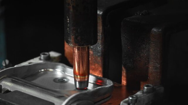 Close-up copper spot welding electrode contacting stamped steel automotive component in oxidized fixture under low-key light, showing precise industrial contact and metal surface detail