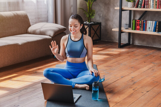 Online sport training, young woman sitting on floor and talking with coach by laptop at home, fit female exercising remotely, fitness and wellness concept