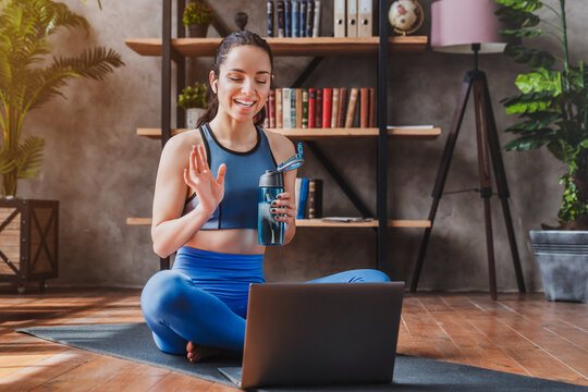 Young woman doing sports on mat with laptop during online classes at home, fit female exercising indoors, virtual workout, wellness and healthy lifestyle concept