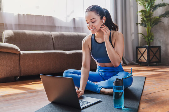 Sport and recreation concept, sporty woman in sportswear and earphones working out while using laptop in living room at home, fitness and wellness lifestyle