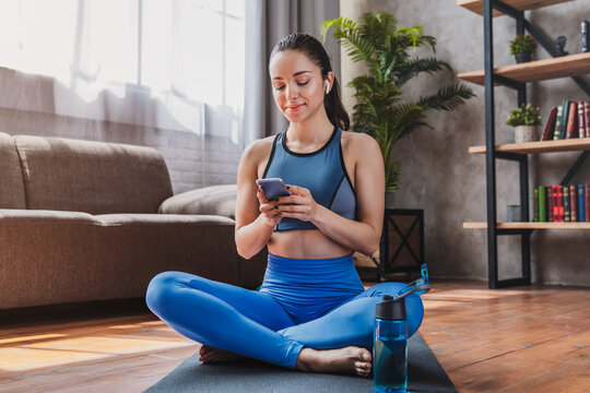 Beautiful woman in headphones looking at smartphone, listening to music and relaxing after training, fit female enjoying audio, fitness and wellness lifestyle concept