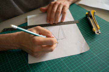Naklejka premium An engineer focuses on drawing a design with a pencil and ruler on paper while seated at a table in a workspace