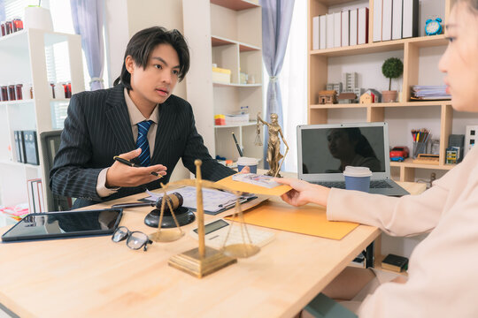 An Asian businessman hands an envelope containing money to a lawyer as payment for legal services; a concept regarding bribery and corruption.