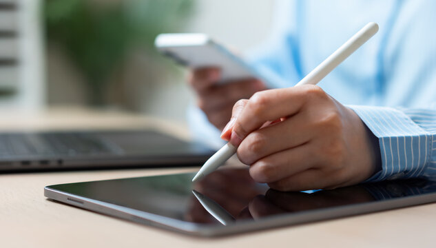 Businesswoman using a stylus pen on a digital tablet while holding a smartphone, representing electronic signatures, digital documentation, paperless workflows, business technology, and productivity.