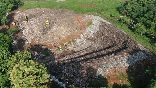 Aerial drone footage of two excavators operating on the active landfill cell at a waste disposal site. Slow, stable landscape video showcasing landfill operations, environmental services,