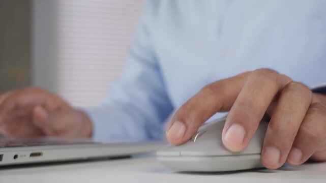 Close-up of business professional using wireless computer mouse beside laptop for digital office work, online productivity, remote workflow, data management, and modern workplace technology