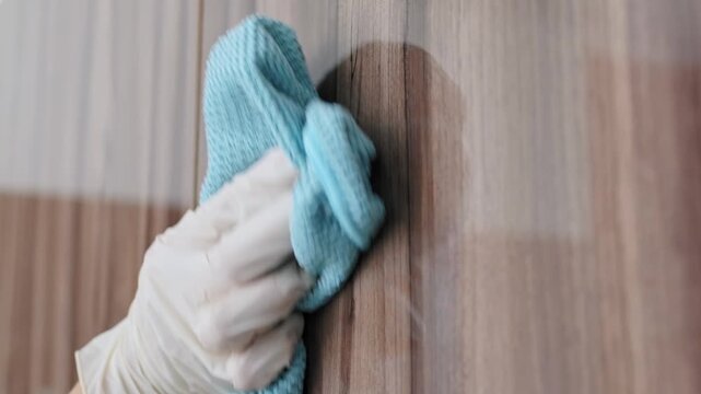 Close-up of gloved hand cleaning wooden surface using microfiber cloth for spotless results. Surface care emphasizes cleaning quality, hygienic maintenance, professional housekeeping and interior upke