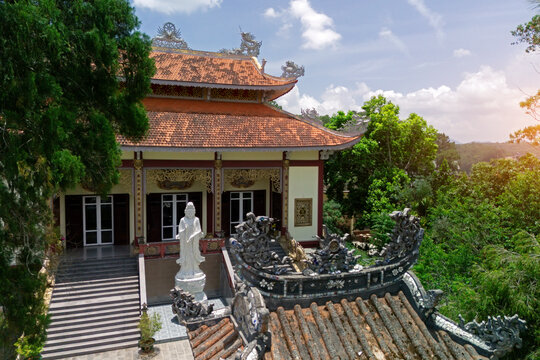Grand Buddhist temple with multiple red-orange tiled roofs and a tall white Quan Am statue standing at the entrance steps