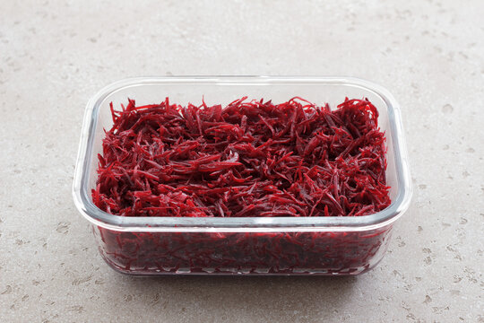 Fresh grated beetroot salad in a glass food container with fork on a light stone surface. Healthy vegetable dish, meal prep ingredient