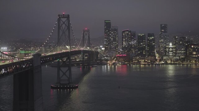 Glowing San Francisco Downtown Skyline Across Bay Near Beautiful Bridge at Night - Aerial Shot