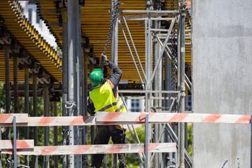 Naklejka premium Construction worker secures scaffolding at a building site during daytime in a city