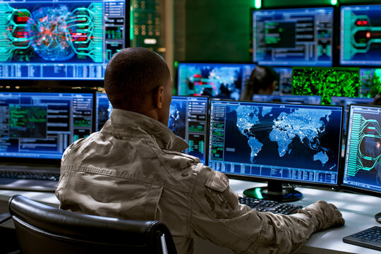 Military cybersecurity specialist monitoring global network activity in advanced security operations center with multiple intelligence displays