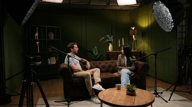 Man and woman recording a podcast interview sitting on a couch in a professional studio