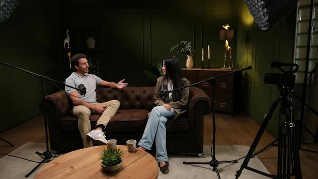 Two people, a man and a woman, are sitting on a couch talking during an interview for a podcast