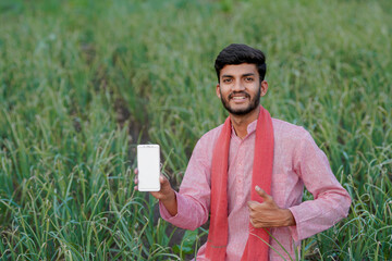 young indian farmer showing smartphone screen sitting at green agricultural field © Niks Ads