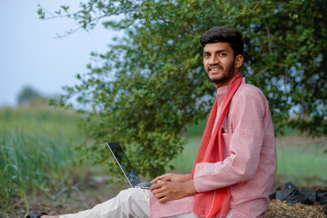 Obraz premium young indian farmer holding laptop standing at agricultural field