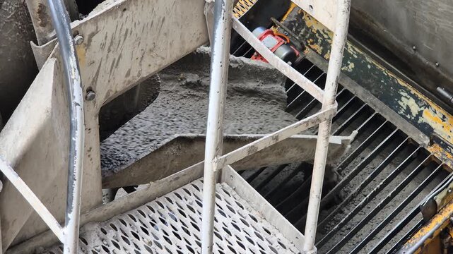 Slow motion diagonal high angle view of fresh concrete pouring from a mixer truck chute into a pump hopper