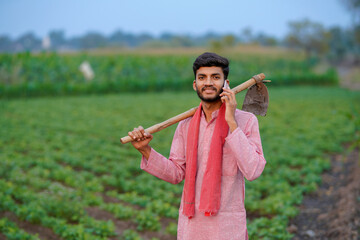 Fototapeta premium young indian farmer holding farming tool standing at field