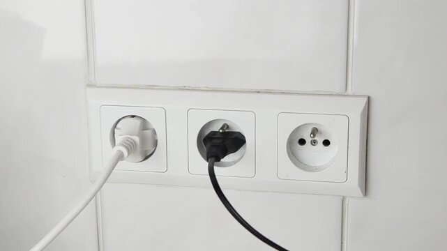 Close-up of a female hand plugging an electrical power plug into a wall socket. Everyday household action showing connecting an electronic device to the power supply, home electricity.