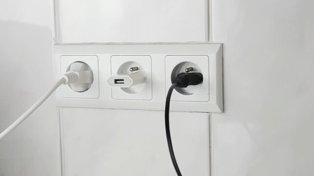 Close-up of a female hand plugging an electrical power plug into a wall socket. Everyday household action showing connecting an electronic device to the power supply, home electricity.