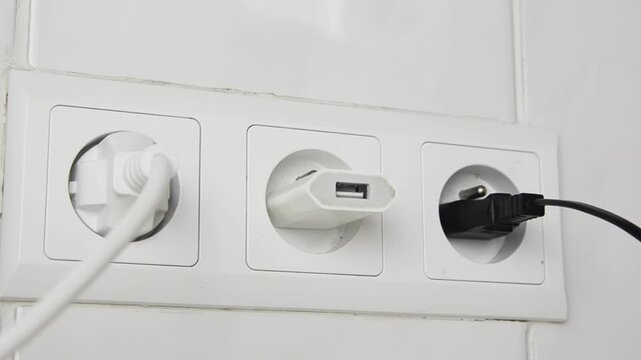 Close-up of a female hand unplugging one USB cable from a wall power adapter and connecting another cable. Everyday technology concept showing charging accessories, USB connection.
