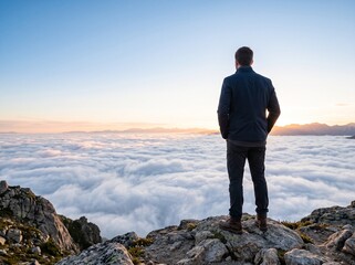Fototapeta premium Man in a navy blazer stands on a rocky mountain peak overlooking clouds during sunset