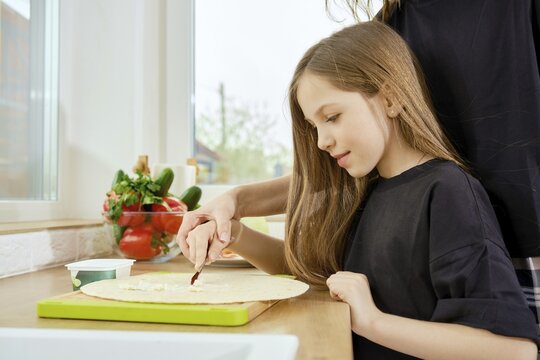 Young girl under the guidance of her mother spreads cream cheese on a flatbread with spreader knife