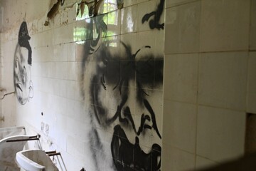 Abandoned bathroom with old sink and dark graffiti mural on tiled wall © Hicham