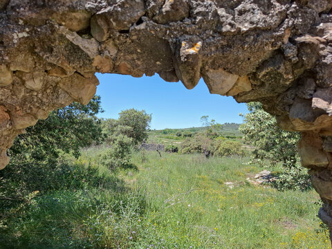 Scenic view through ancient stone window showing a lush meadow and distant hills on a sunny day