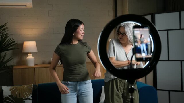 Happy grandmother and granddaughter dancing at home while recording a video for social media