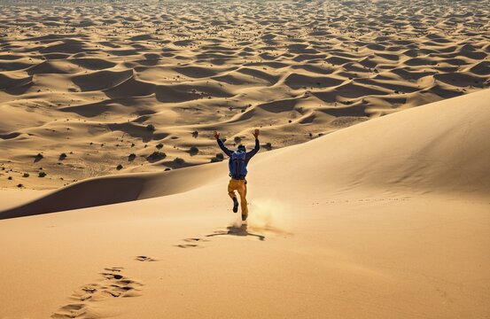 Young man walking down a sand dune, dune landscape Erg Chebbi, Merzouga, Sahara, Morocco