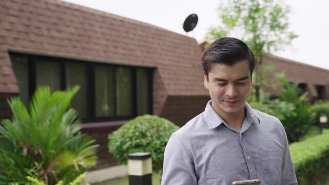 Portrait of happy handsome Caucasian businessman in a shirt holding and using a smartphone while walking on the street outdoors in a public park. A young white male uses a mobile phone in a village. 