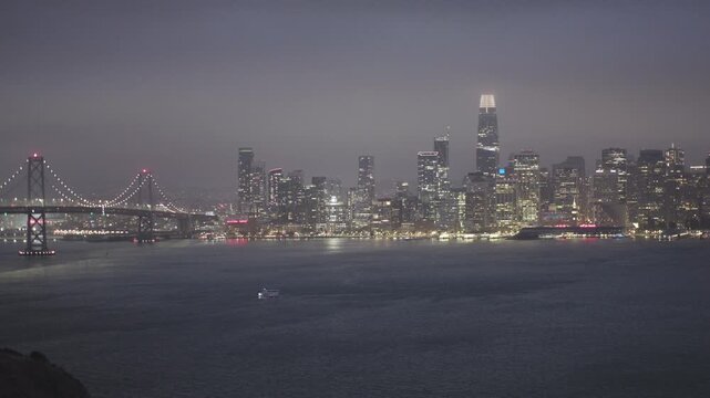 Sparkling San Francisco Skyline And Bridge at Night With Boat in Bay - Wide, Aerial Shot