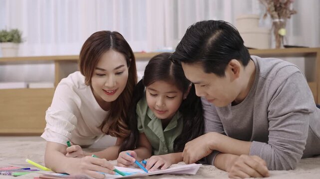 Happy Asian Family Day Concept. Smiling father mother and daughter relaxing and painting on paper together in living room at home. Activity leisure of dad mom and child girl cheerful and fun to draw. 