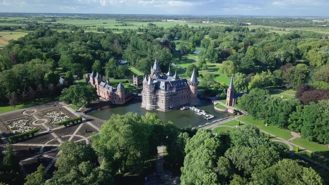Aerial backwards movement showing Haar Castle surrounded by a moat and a lush green park in the Netherlands on a sunny day