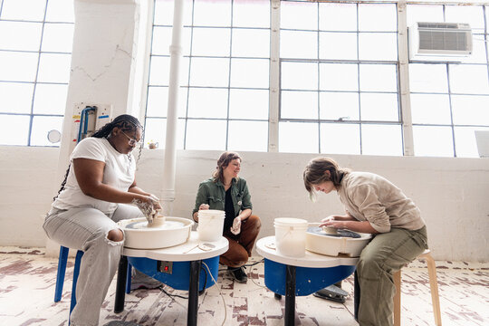 Instructor Watching Two Teens Throw Clay on Pottery Wheels in Studio