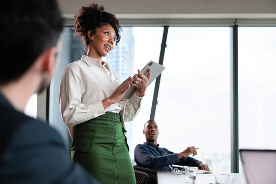 Businesswoman presents with tablet to colleagues in modern office.