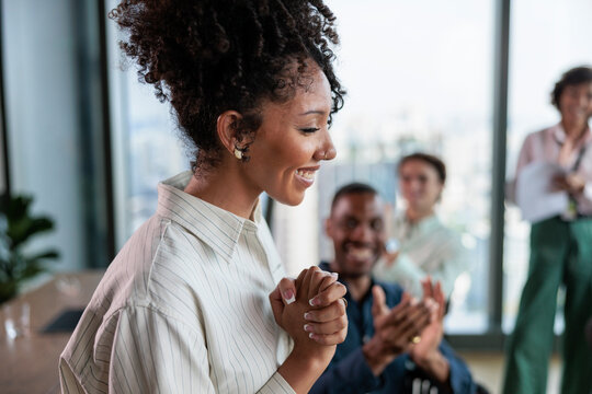 Woman smiles as colleagues applaud in modern office setting.