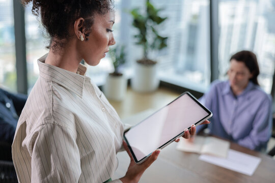 Businesswoman presents tablet to colleague in modern office setting.