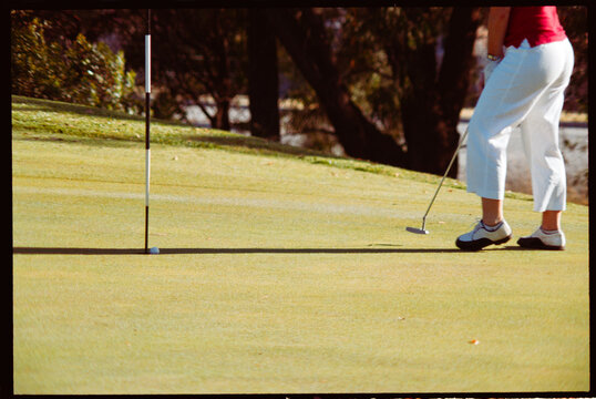 Woman Putts Golf Ball on Green in Sunny Weather During the Day