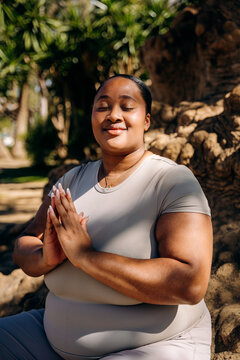 A woman meditates sitting on the root of a tree