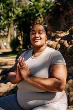 A woman meditates sitting on the root of a tree