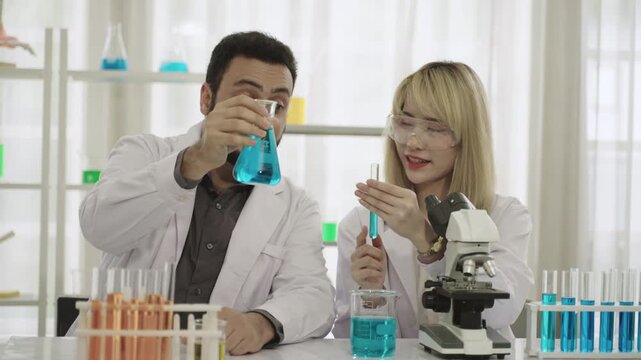 Male and female scientists and researchers in lab coats with microscope are conducting chemistry experiments with liquid in test tubes and beakers in laboratory. Two chemistry experts working in lab. 