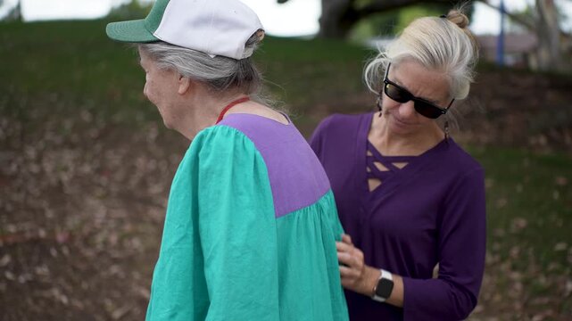 Mature daughter massages her elderly mothers back in a park as they talk, smile, and share stories during their visit and time together