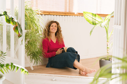 Woman enjoys reading while surrounded by houseplants on balcony