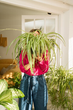 A woman stands on a balcony holding a large houseplant