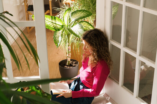 Woman enjoying a book on the balcony surrounded by houseplants